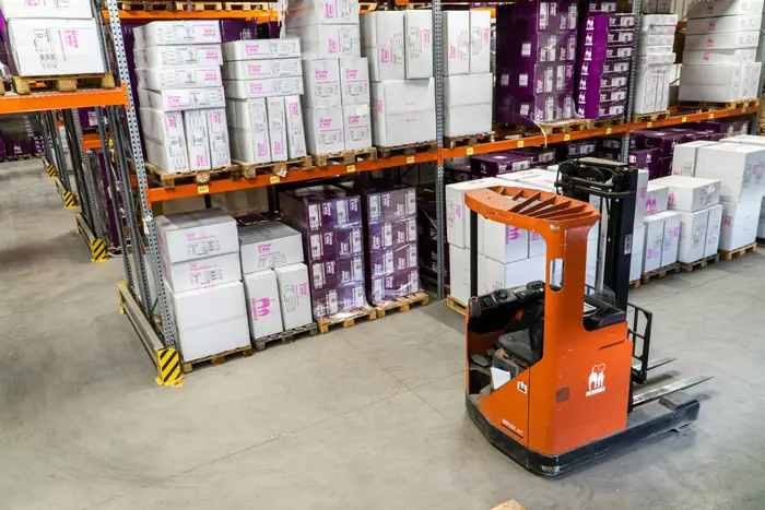Forklift moving cartons between pallet racks